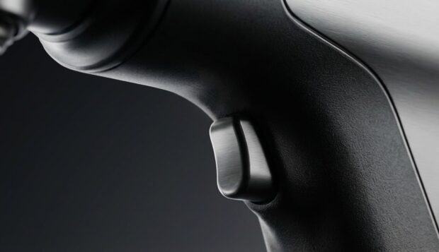 Detailed close-up of the surgical saw’s textured black handle and brushed-metal trigger, with part of the metallic housing visible against a dark background.
