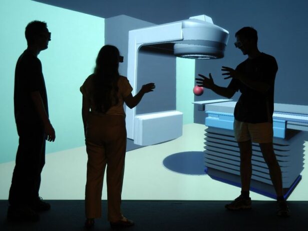 Medical device equipment design on large visualization screen. The silhouettes of three people in foreground, reviewing the image on the screen.