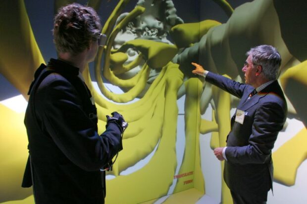 two men standing in a CAVE environment reviewing an enlarged skeleton on the display.